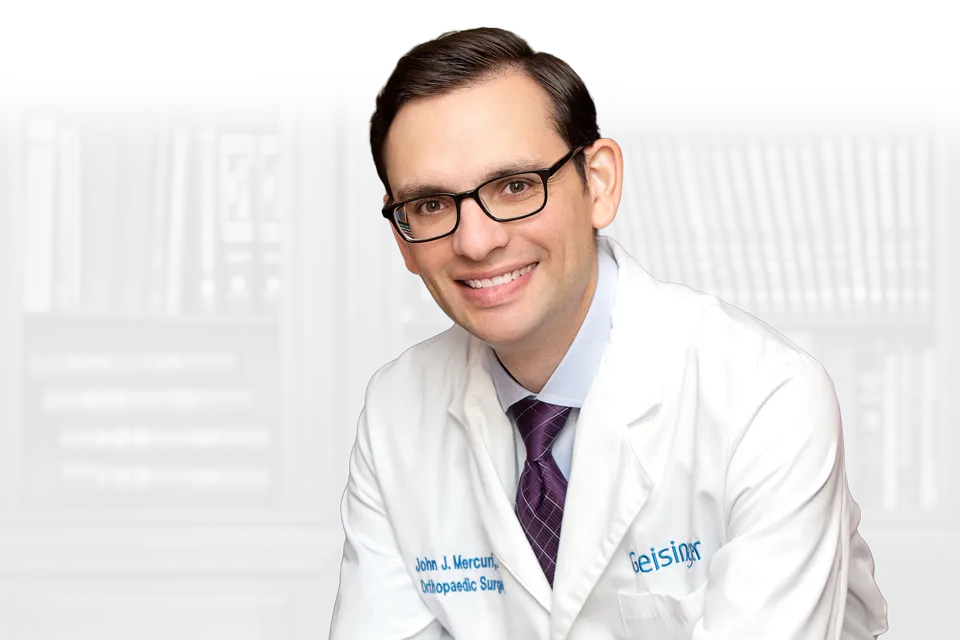 Dr. John J. Mercuri smiling in front of a wall of medical books